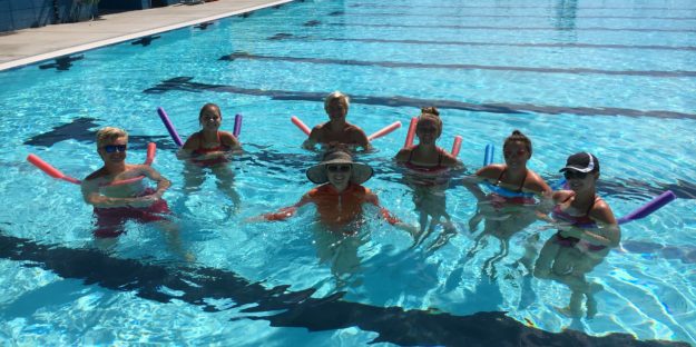 Nina and six students standing in a pool and smiling